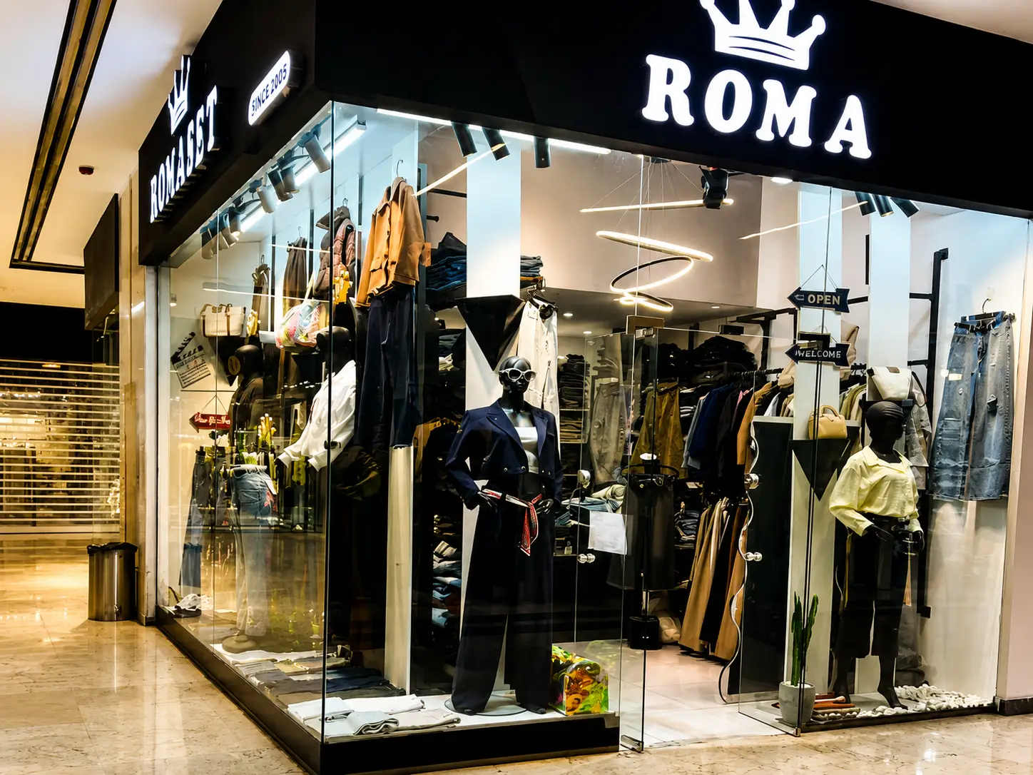 نمای بیرونی فروشگاه پوشاک زنانه ROMA با ویترین شیشه‌ای، مانکن‌های مدرن و نورپردازی سرد و رسمی در مرکز خرید